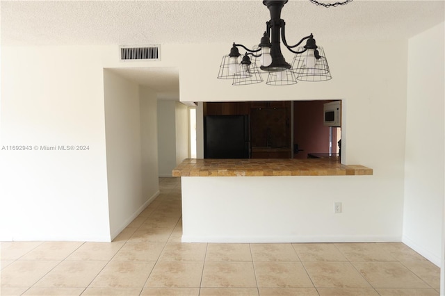 kitchen with light tile patterned floors, a textured ceiling, an inviting chandelier, and black fridge