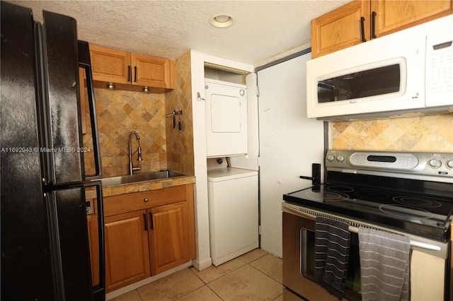 kitchen featuring black refrigerator, stacked washing maching and dryer, tasteful backsplash, light tile patterned floors, and stainless steel electric range oven