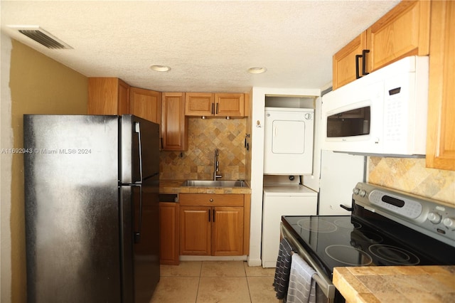 kitchen featuring tasteful backsplash, black fridge, stainless steel range with electric cooktop, sink, and stacked washer / drying machine