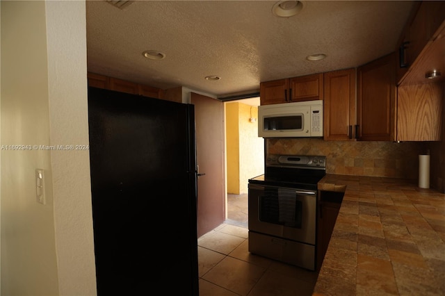 kitchen with stainless steel electric stove, decorative backsplash, black refrigerator, and a textured ceiling