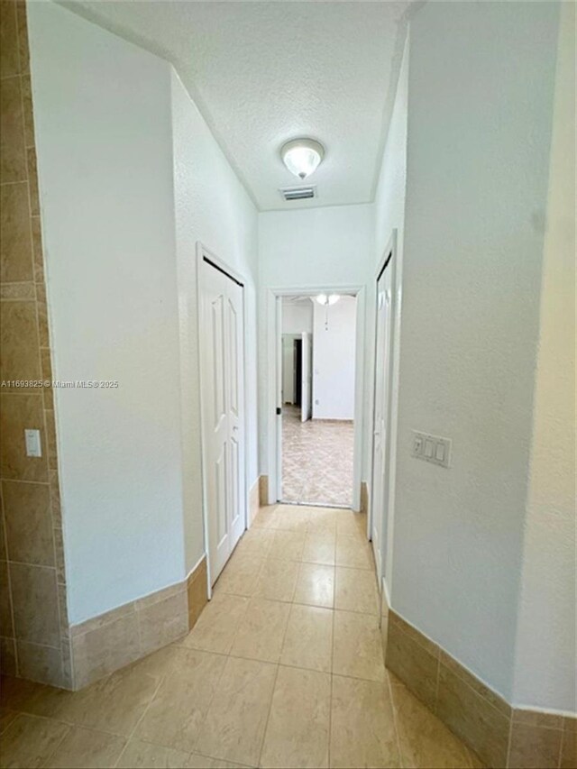 hall featuring light tile patterned flooring and a textured ceiling