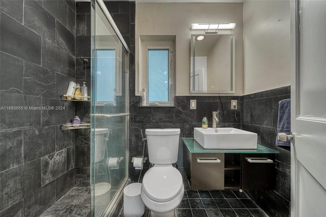 bathroom featuring tile patterned floors, toilet, vanity, a shower with shower door, and tile walls