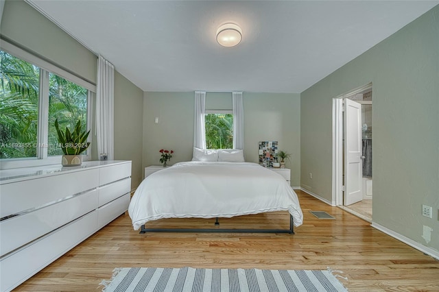 bedroom with light hardwood / wood-style floors, connected bathroom, and multiple windows