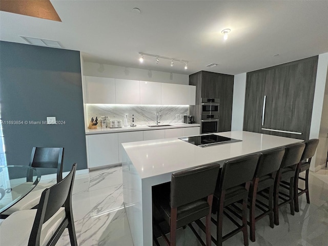 kitchen with black electric cooktop, double oven, sink, white cabinets, and a center island