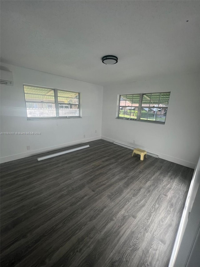 empty room featuring an AC wall unit, dark hardwood / wood-style flooring, and a healthy amount of sunlight