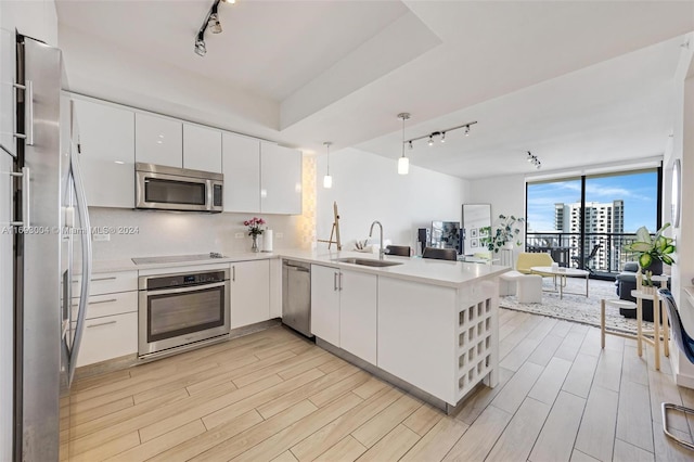 kitchen with stainless steel appliances, kitchen peninsula, decorative light fixtures, white cabinets, and light wood-type flooring