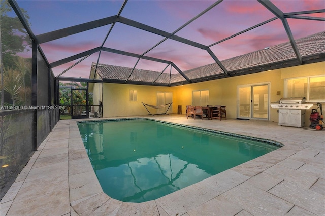 pool at dusk with glass enclosure and a patio