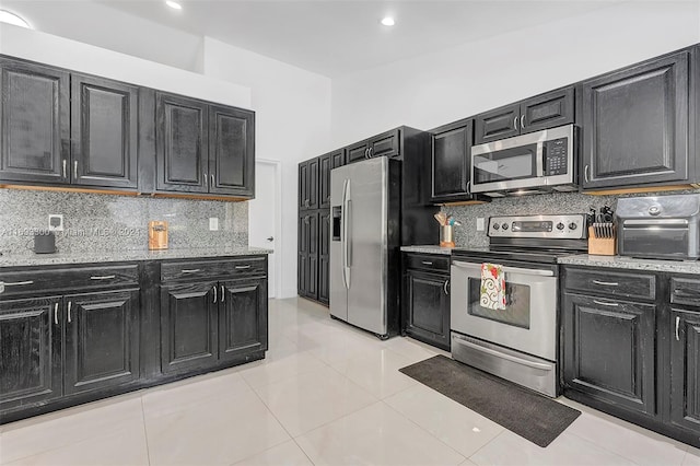 kitchen featuring light stone countertops, decorative backsplash, light tile patterned floors, and stainless steel appliances