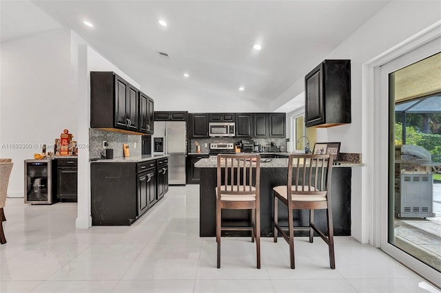 kitchen with beverage cooler, stainless steel appliances, light stone counters, vaulted ceiling, and a kitchen bar