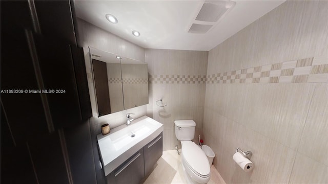 bathroom featuring tile patterned flooring, vanity, tile walls, and toilet