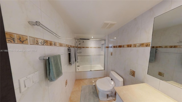 full bathroom featuring vanity, bath / shower combo with glass door, tile patterned flooring, toilet, and tile walls