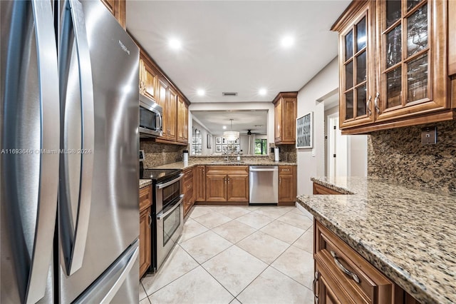 kitchen with hanging light fixtures, light tile patterned floors, light stone countertops, tasteful backsplash, and stainless steel appliances