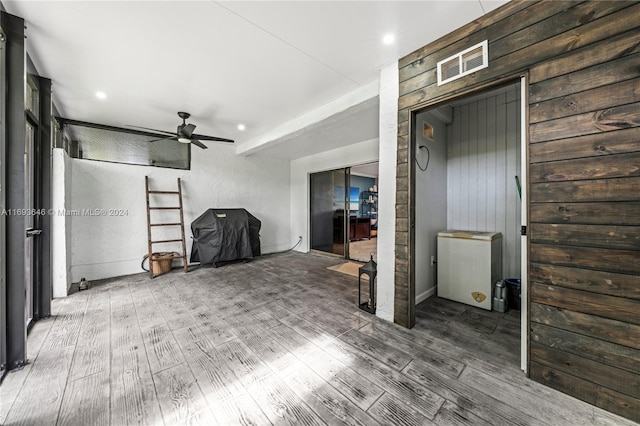 unfurnished living room with hardwood / wood-style flooring, ceiling fan, and wood walls