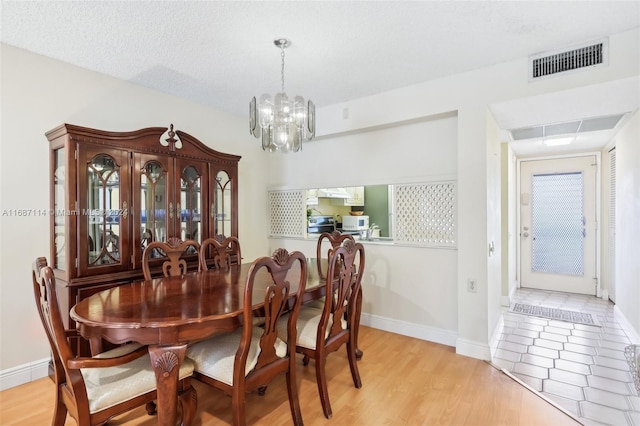 dining area featuring light wood-type flooring, a textured ceiling, and a chandelier