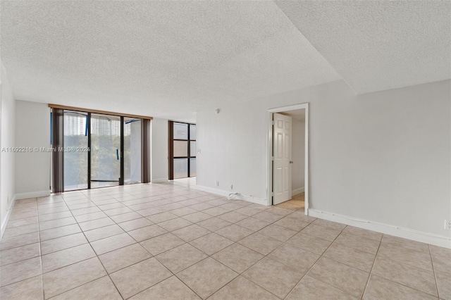 empty room featuring expansive windows, light tile patterned flooring, and a textured ceiling