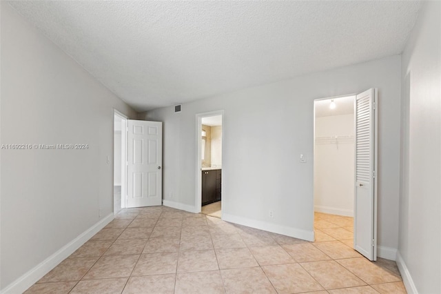 unfurnished bedroom featuring light tile patterned floors, ensuite bathroom, a spacious closet, and a closet