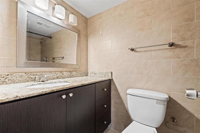 bathroom featuring walk in shower, vanity, toilet, and tile walls