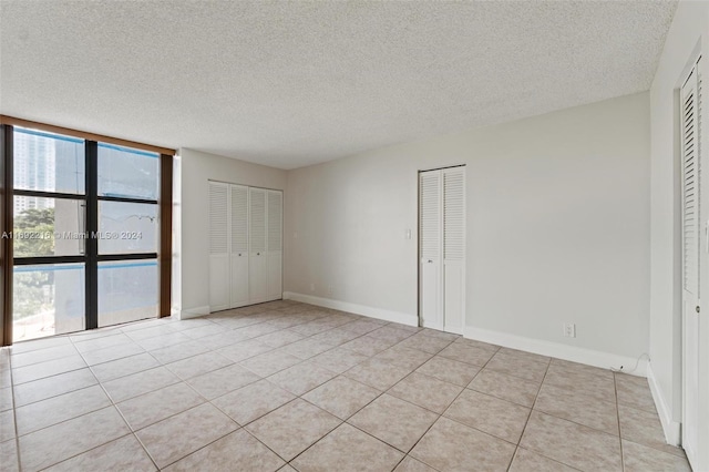 unfurnished bedroom featuring a textured ceiling, multiple windows, and two closets