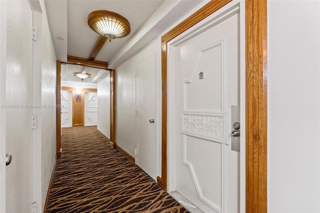 corridor with dark carpet and a textured ceiling