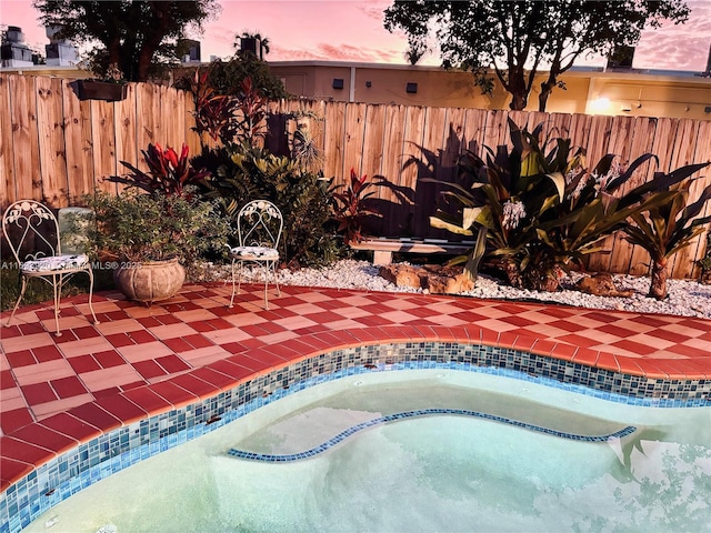 pool at dusk with a hot tub