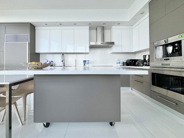 kitchen featuring white cabinetry, sink, wall chimney range hood, a kitchen breakfast bar, and a kitchen island