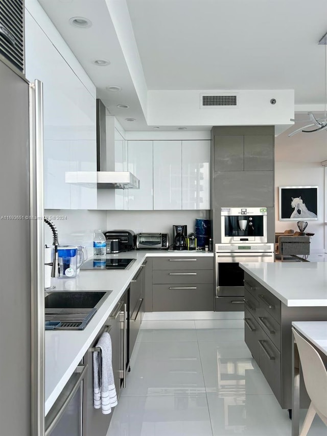 kitchen featuring gray cabinetry, wall chimney exhaust hood, light tile patterned floors, and stainless steel appliances