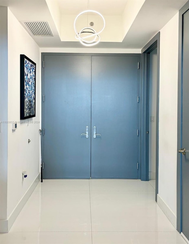 hallway with a tray ceiling and light tile patterned flooring