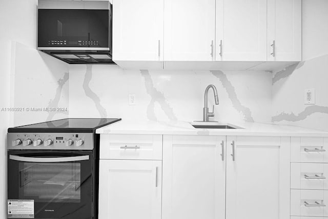 kitchen featuring white cabinetry, light stone counters, electric stove, and sink