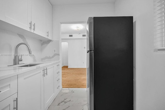 kitchen featuring white cabinets, stainless steel fridge, light hardwood / wood-style flooring, and sink