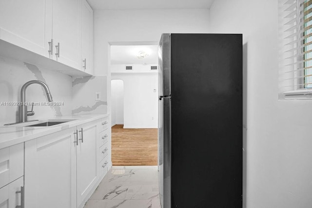 kitchen with white cabinetry, sink, tasteful backsplash, light hardwood / wood-style flooring, and stainless steel fridge