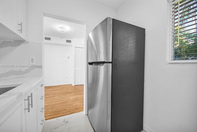 kitchen with light stone countertops, stainless steel fridge, light wood-type flooring, and white cabinetry