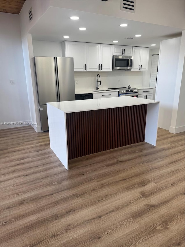 kitchen featuring appliances with stainless steel finishes, sink, white cabinets, a center island, and light hardwood / wood-style floors