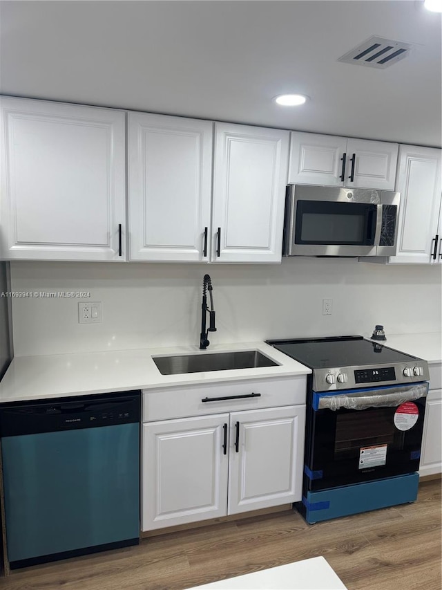 kitchen with sink, white cabinets, stainless steel appliances, and hardwood / wood-style flooring