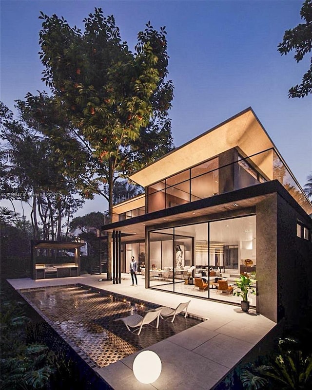 back house at dusk featuring outdoor lounge area, a patio area, a balcony, and a swimming pool