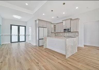 kitchen featuring white fridge, light hardwood / wood-style floors, an island with sink, gray cabinets, and decorative backsplash