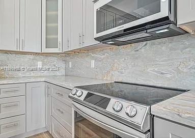 kitchen featuring white cabinets, backsplash, light stone countertops, and stainless steel appliances