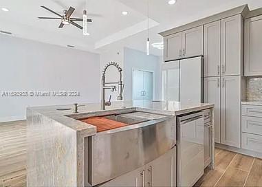 kitchen with gray cabinets, a kitchen island with sink, white refrigerator, and light wood-type flooring