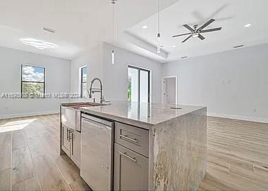 kitchen featuring light stone countertops, light wood-type flooring, stainless steel dishwasher, a kitchen island with sink, and ceiling fan