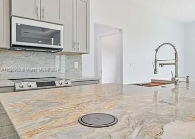 kitchen with light stone countertops, appliances with stainless steel finishes, gray cabinetry, and sink