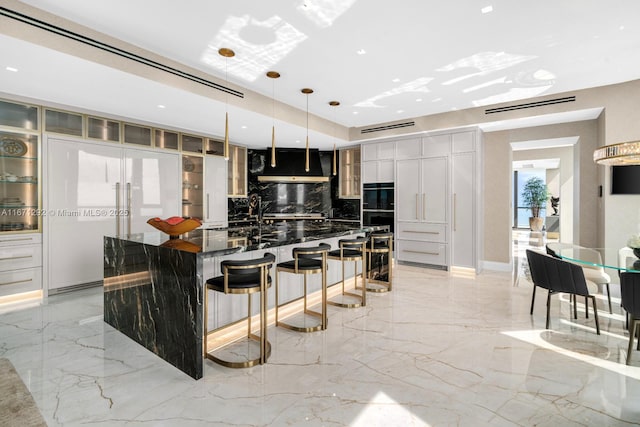 kitchen featuring tasteful backsplash, ventilation hood, hanging light fixtures, dark stone countertops, and a large island