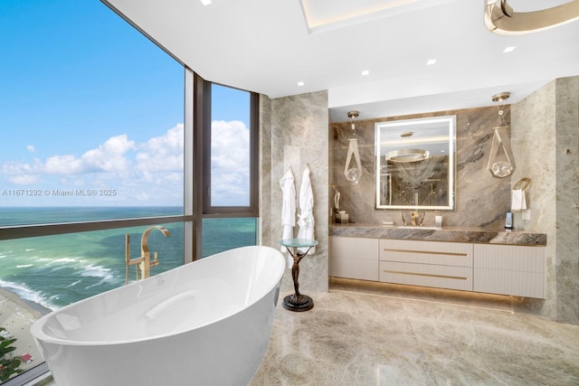 bathroom featuring vanity, a water view, floor to ceiling windows, and a tub to relax in