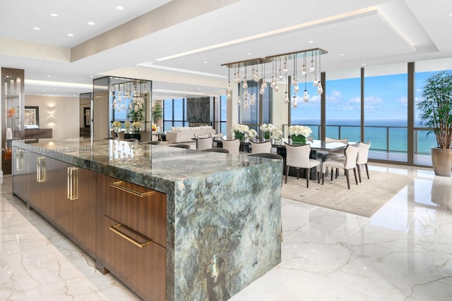 kitchen with a water view, dark stone countertops, a tray ceiling, expansive windows, and a large island