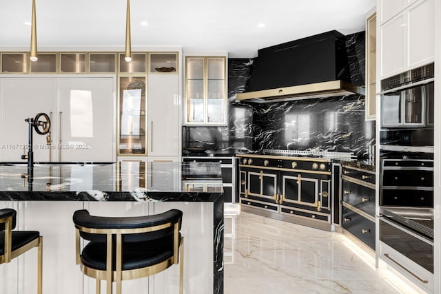 kitchen with decorative light fixtures, stainless steel gas stovetop, a kitchen breakfast bar, dark stone counters, and wall chimney range hood