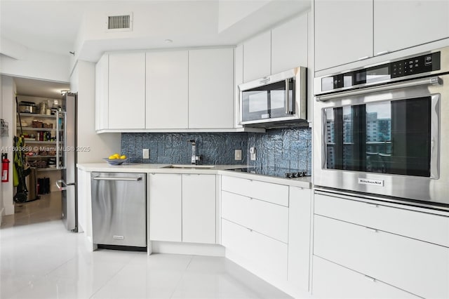 kitchen with appliances with stainless steel finishes, tasteful backsplash, sink, light tile patterned floors, and white cabinetry