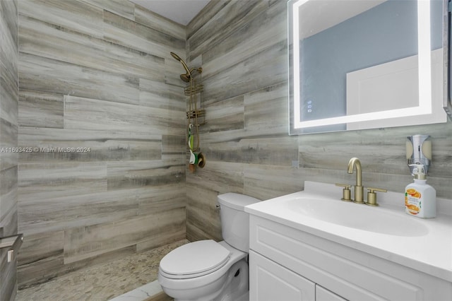 bathroom with tiled shower, vanity, toilet, and tile walls