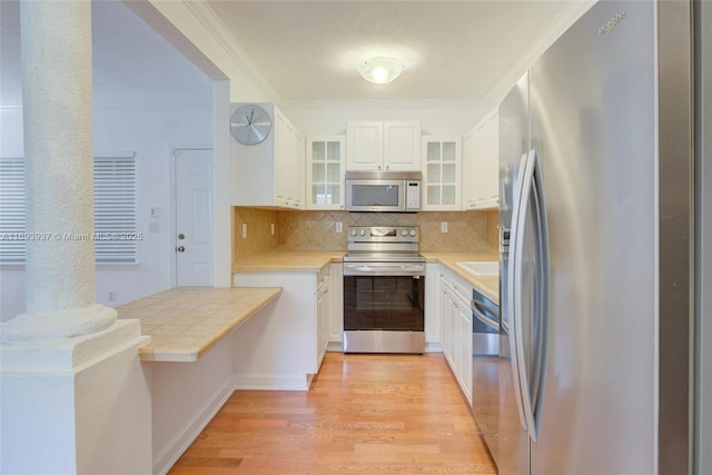 kitchen featuring white cabinets, crown molding, light hardwood / wood-style flooring, appliances with stainless steel finishes, and tasteful backsplash