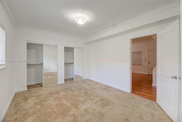 unfurnished bedroom with crown molding, light colored carpet, and two closets