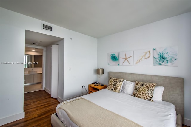 bedroom with dark wood-type flooring and connected bathroom