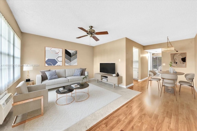 living room featuring a wall mounted air conditioner, ceiling fan, a textured ceiling, and light hardwood / wood-style flooring