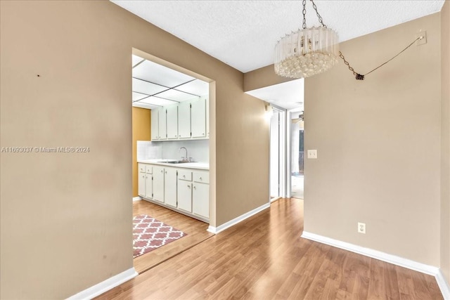 unfurnished dining area with sink, light wood-type flooring, a textured ceiling, and an inviting chandelier